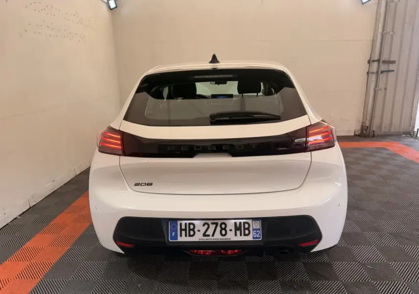 Vue arrière d'une Peugeot 208 blanche 2025 dans un garage, avec feux arrière allumés et plaque d'immatriculation visible.