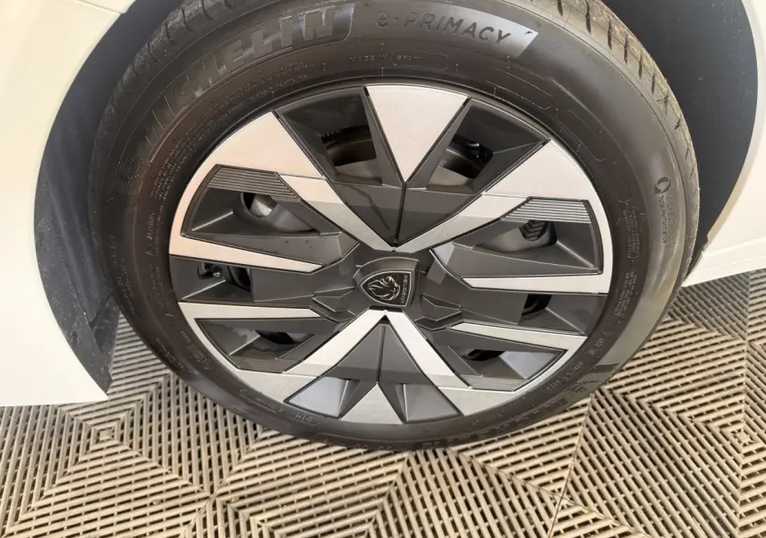 Gros plan sur la roue avant droite blanche d'une Peugeot 208 2025 avec jante au design géométrique noir et argent.