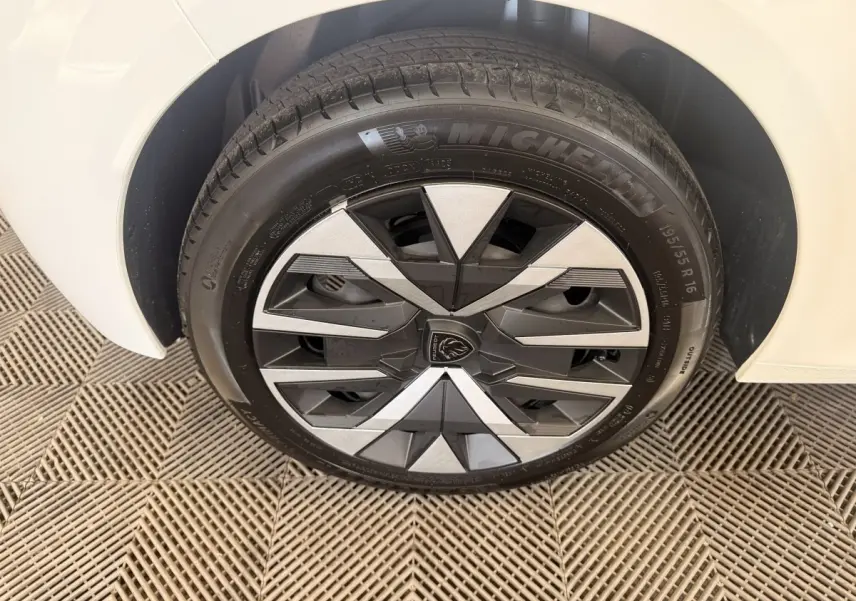 Gros plan sur la roue avant droite blanche d'une Peugeot 208 2025 avec jante au design géométrique noir et argent.
