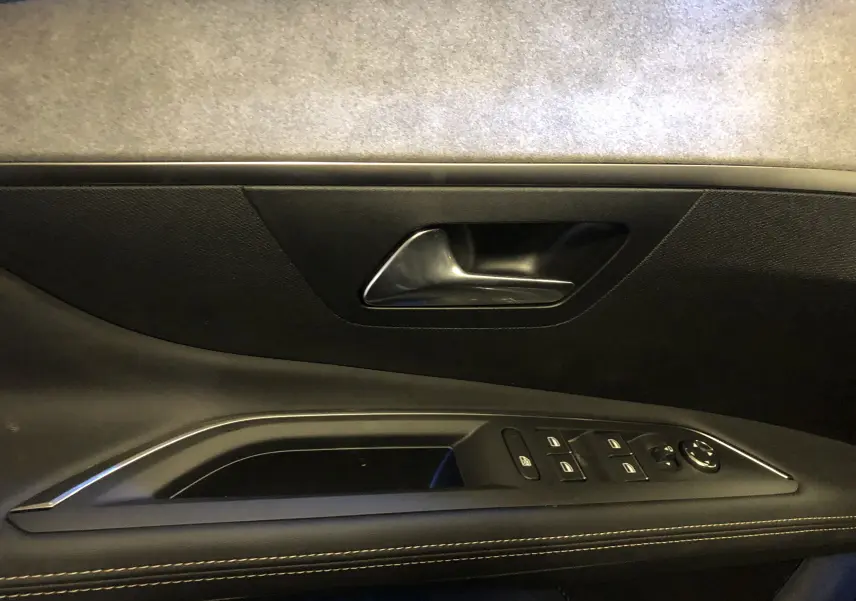 Gros plan sur la poignée intérieure et les commandes de la porte côté conducteur du Peugeot 3008 GT gris platinium toit noir.