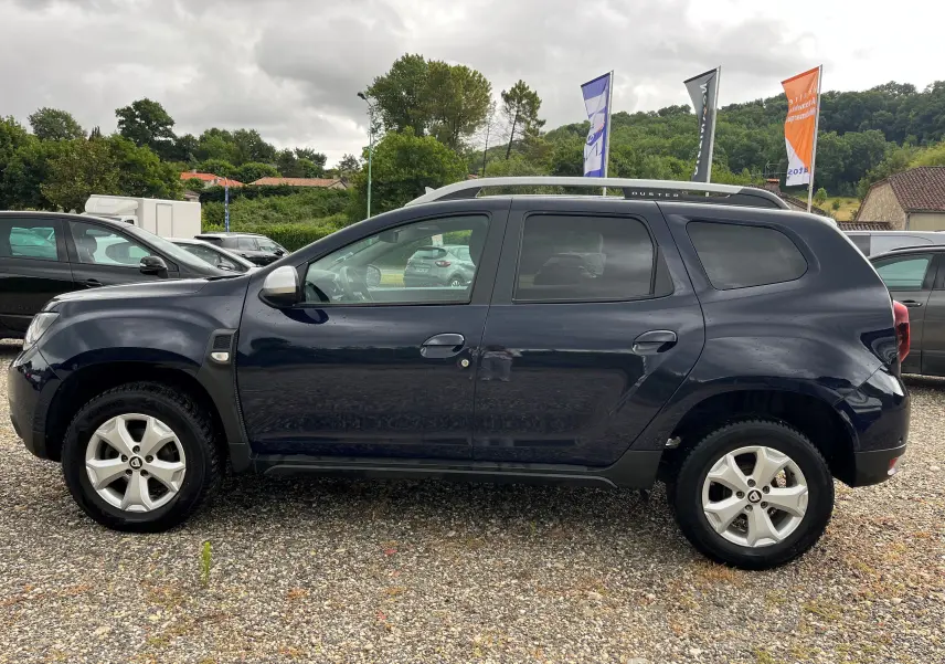 Profil côté gauche du Dacia Duster 1.5 DCI bleu marine 2018 avec barres de toit et jantes alliage visibles.