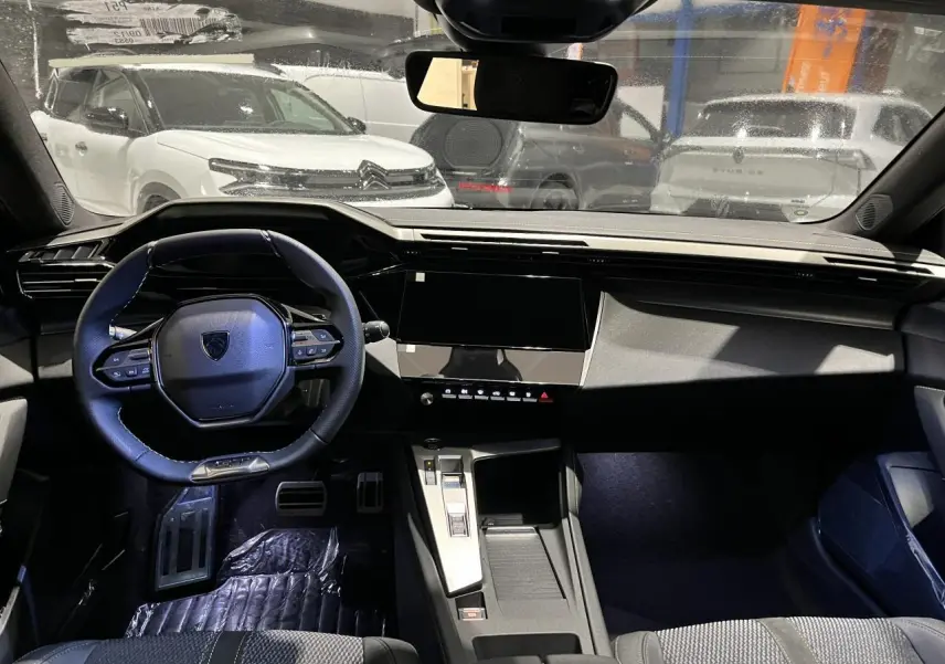Vue intérieure avant du poste de conduite d'une Peugeot 308 2024 avec volant compact et tableau de bord moderne noir.