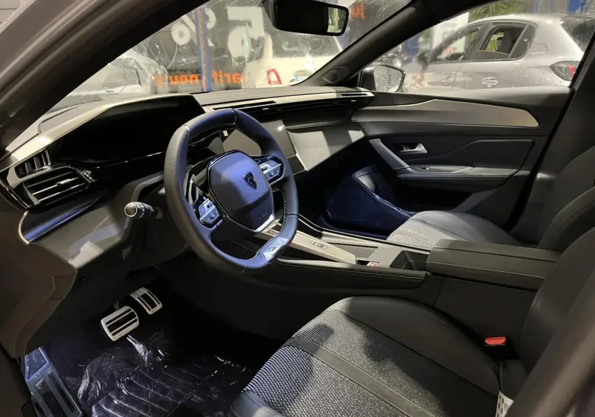 Intérieur avant droit de la Peugeot 308 2024, volant cuir, sellerie tri-matières et planche de bord moderne noire.