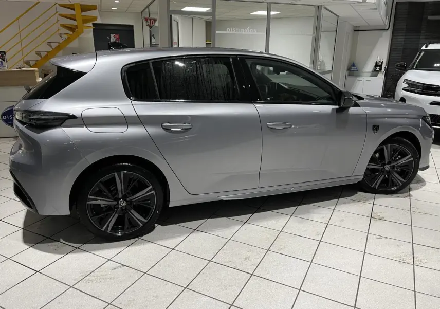 Peugeot 308 Gris Artense vue de profil côté gauche en intérieur avec jantes alliage noires et vitres surteintées.