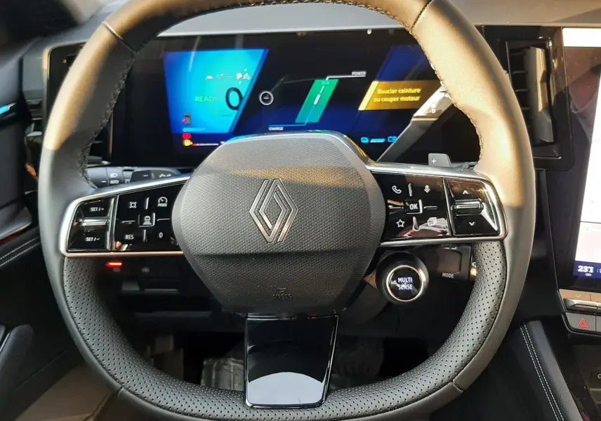 Volant cuir noir avec logo Renault au centre, tableau de bord numérique et commandes intégrées, intérieur Renault Austral 2025.