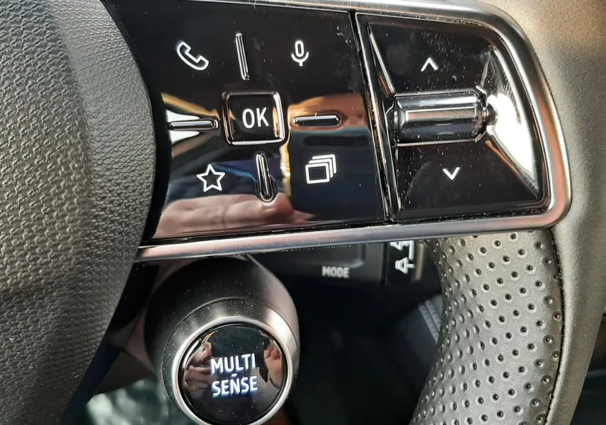 Gros plan sur les commandes au volant noir perforé du Renault Austral 2025, avec bouton Multi-Sense et touches tactiles.