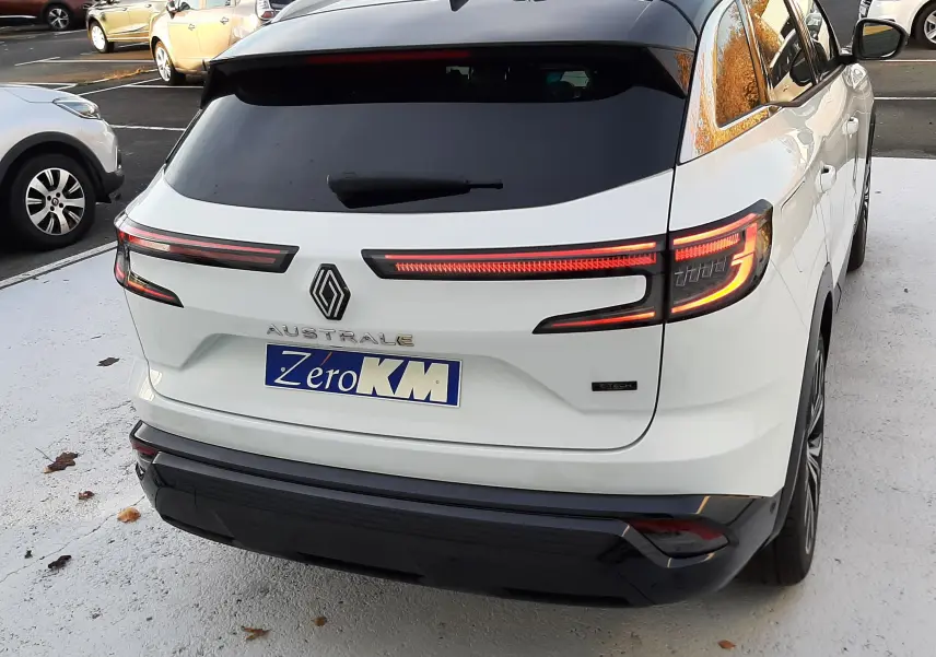 Vue 3/4 arrière droite d'un Renault Austral blanc nacré avec toit noir, feux arrière LED allumés et plaque Zero KM.