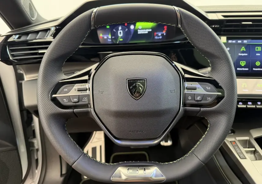 Vue rapprochée du volant cuir noir avec logo Peugeot et badge GT, tableau de bord digital et écran tactile visibles.