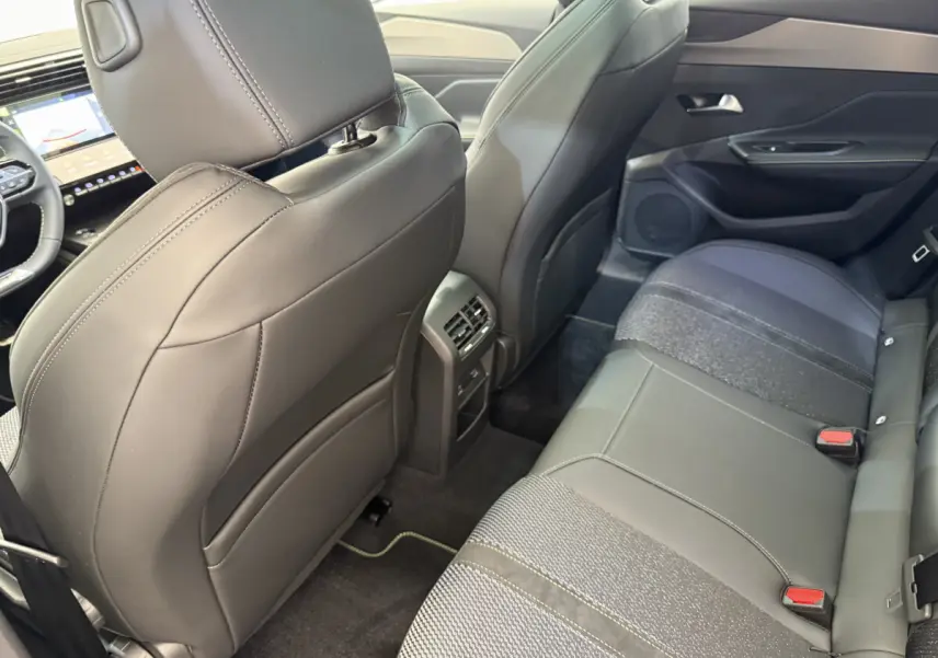Vue intérieure arrière droite de la Peugeot 308 Hybrid 136 e-DCS6 GT 2024, sièges en cuir noir et tissu gris.