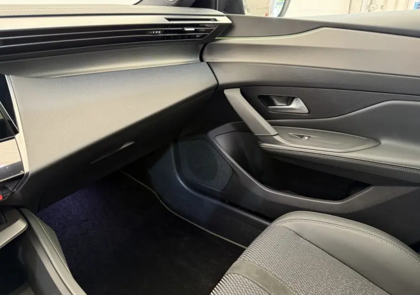 Intérieur côté passager de la Peugeot 308 Hybrid 136 e-DCS6 GT 2024, avec sellerie grise et tableau de bord noir.