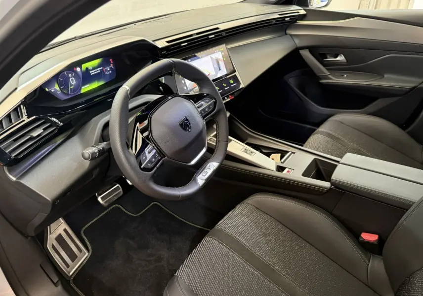 Intérieur noir de la Peugeot 308 Hybrid 136 GT 2024, vue côté conducteur avec tableau de bord digital et volant cuir.