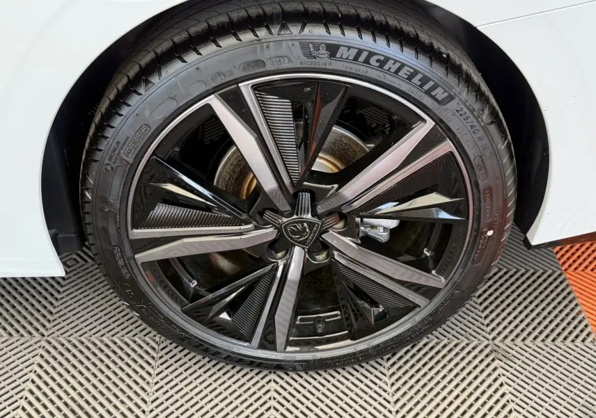 Gros plan sur la roue avant droite d’une Peugeot 308 Hybrid 136 e-DCS6 GT blanche, jante alliage noire et argent.