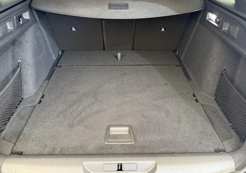 Coffre spacieux de Peugeot 308 Hybrid 136 e-DCS6 GT 2024, vue intérieure arrière avec tapis gris et filets latéraux.