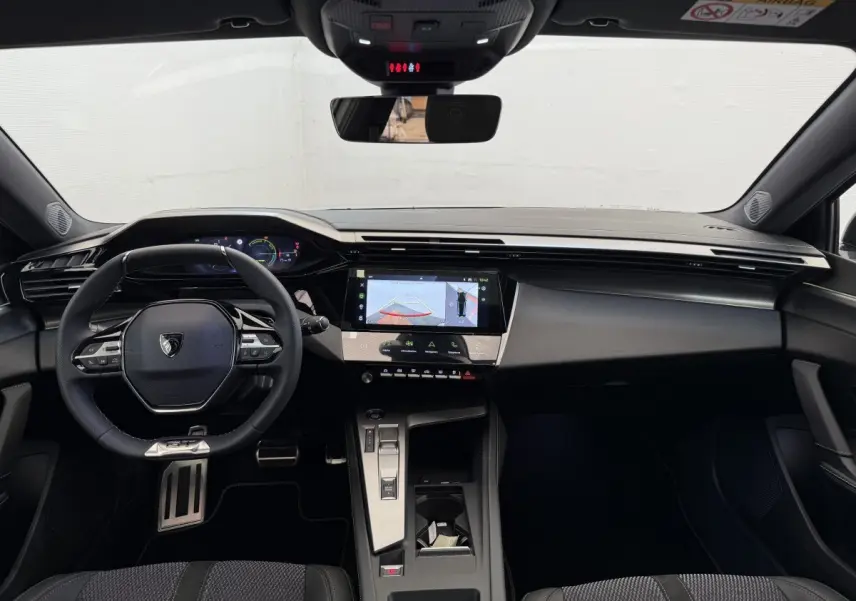 Vue intérieure frontale du tableau de bord de la Peugeot 308 Hybrid 136 e-DCS6 GT 2024 avec écran tactile et volant cuir noir.