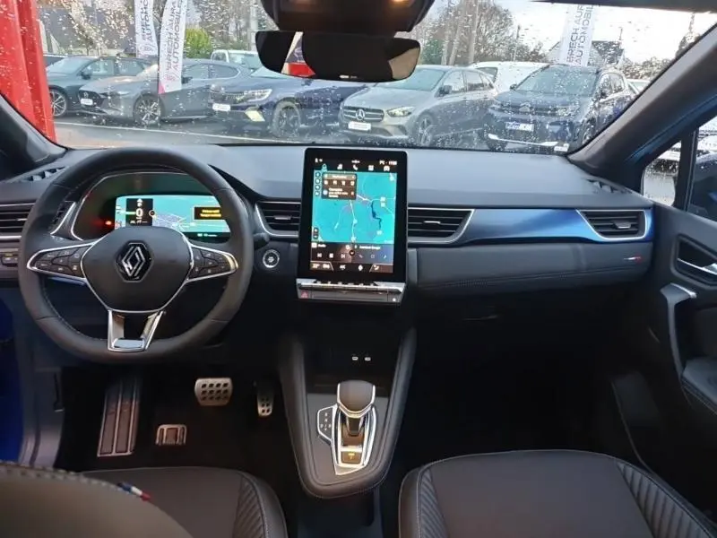 Vue intérieure avant du Renault Captur 2025 Bleu Iron, tableau de bord moderne avec écran tactile vertical et volant cuir multifonction.