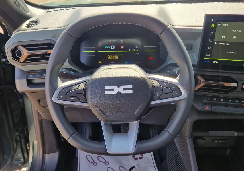 Vue centrée sur le volant et le tableau de bord du Dacia Duster 1.8 Hybrid 155, avec détails orange et écran tactile visible.