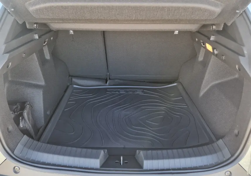 Coffre ouvert du Dacia Duster 1.8 Hybrid 155 en vert cèdre, vue intérieure montrant un tapis de coffre noir texturé.