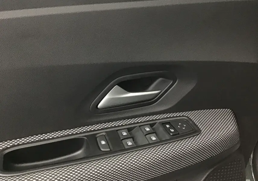 Gros plan sur la commande des vitres et la poignée intérieure côté conducteur d'une Dacia Sandero Stepway kaki 2025.