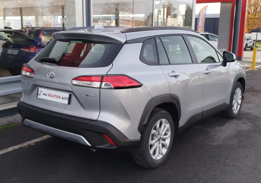 Toyota Corolla Cross 1.8 Hybrid gris acier vue 3/4 arrière droit, avec toit noir et feux arrière LED distinctifs.