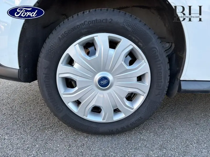 Gros plan sur la roue avant droite d’un Ford Transit Connect blanc glacier avec enjoliveur argenté et logo Ford central.