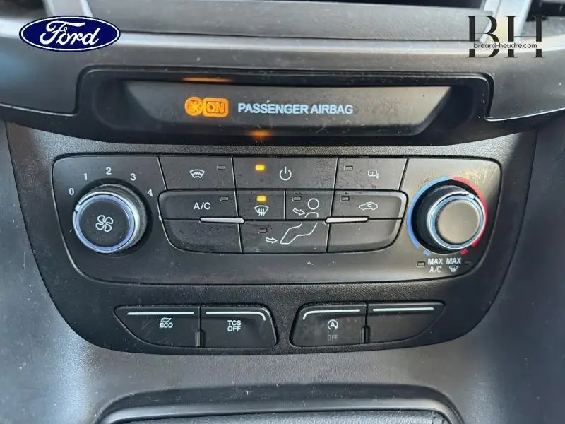 Gros plan sur la console centrale noire du Ford Transit Connect blanc glacier, avec commandes climatisation et témoin airbag passager allumé.
