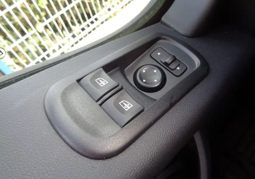 Gros plan sur les commandes de lève-vitres et réglage des rétroviseurs côté conducteur d'un Opel Movano Fourgon blanc polaire.