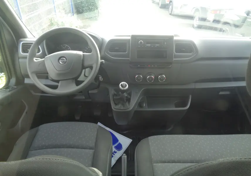 Vue intérieure avant de l'Opel Movano Fourgon 2022 avec tableau de bord noir et volant à gauche, siège tissu gris.