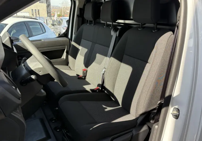 Intérieur de l'Opel Vivaro 2024 vu côté conducteur, montrant la banquette tissu bi-ton noir et gris et le volant réglable.