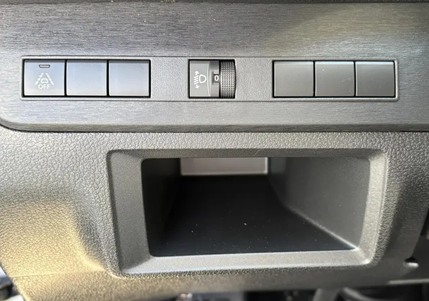 Gros plan sur les commandes noires du tableau de bord de l'Opel Vivaro blanc, avec bouton de réglage des phares et espace de rangement.