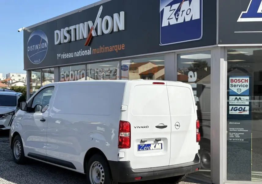 Vue 3/4 arrière droite d'un utilitaire Opel Vivaro blanc stationné devant un garage multimarque.