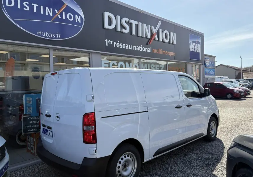 Vue 3/4 arrière droite d’un utilitaire Opel Vivaro blanc stationné devant un concessionnaire Distinxion.