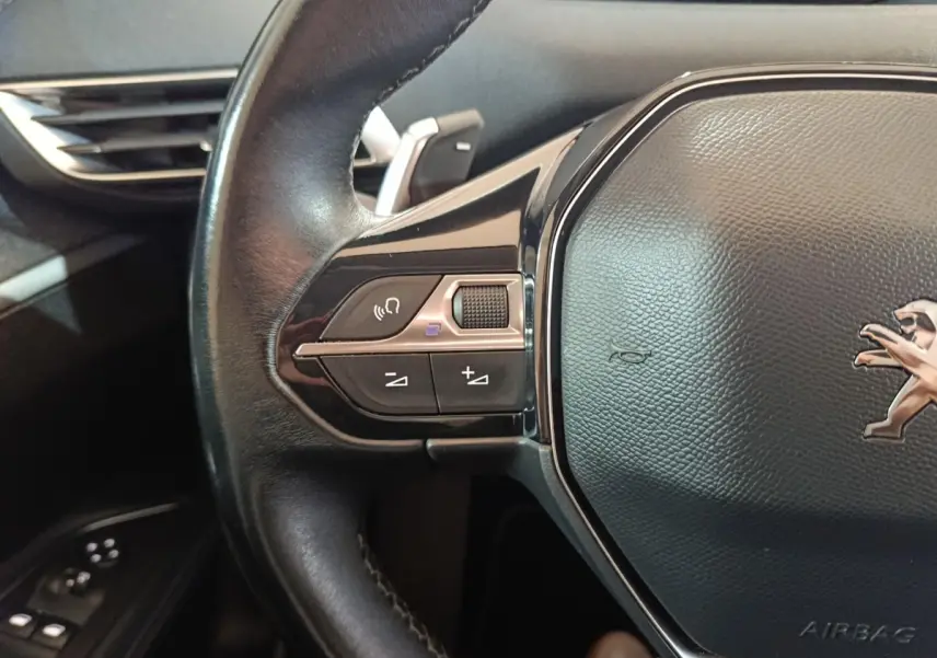 Gros plan sur le volant cuir noir du Peugeot 3008 avec commandes audio et logo lion visible au centre.