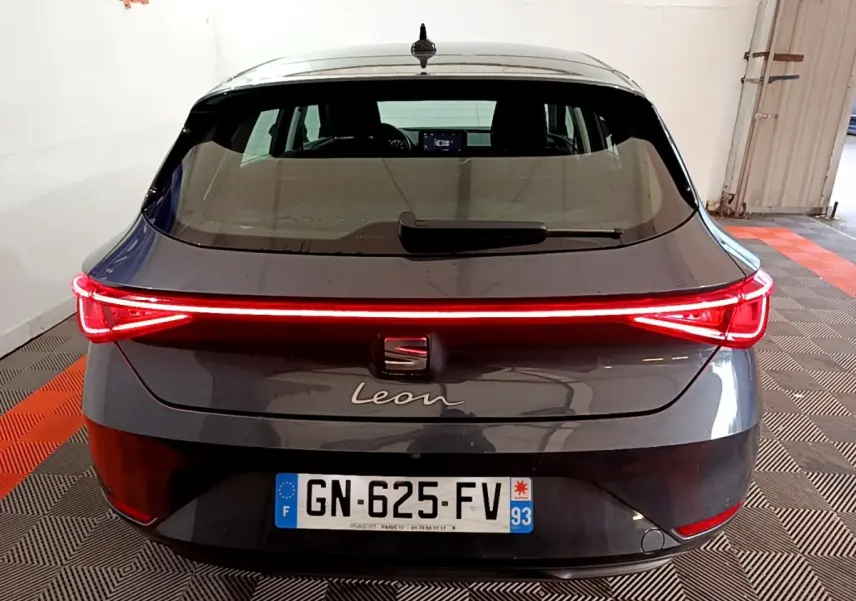 Vue arrière d'une SEAT Leon gris clair 2023 avec feux arrière LED allumés en bande continue rouge.