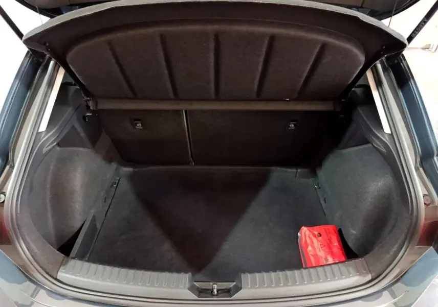 Vue arrière du coffre ouvert d'une SEAT Leon gris clair 2023, avec banquette rabattable et trousse de secours rouge visible.