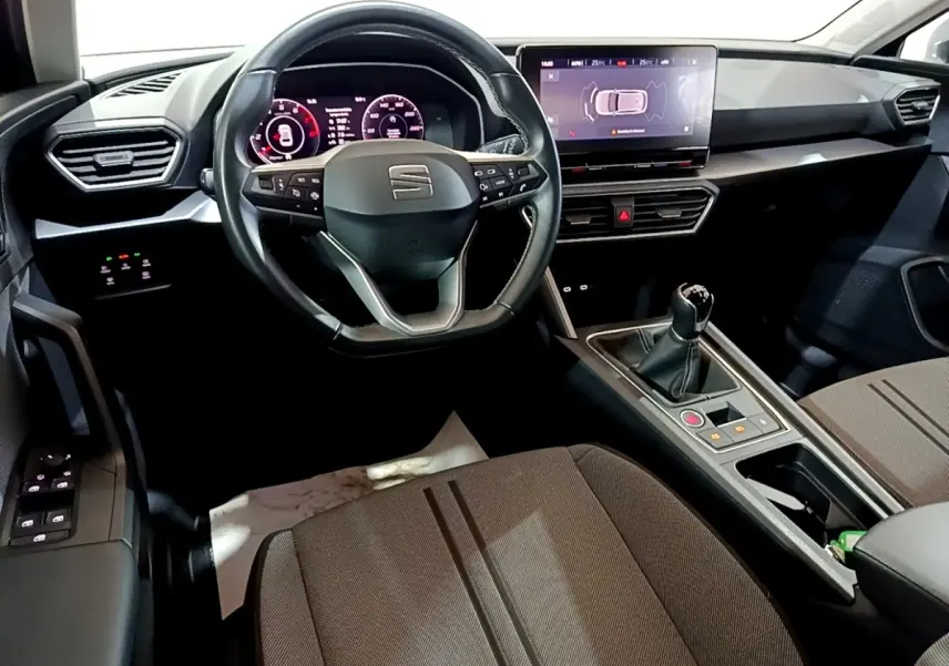 Vue intérieure avant du tableau de bord et volant cuir SEAT Leon 2023 avec écran tactile et boîte manuelle.