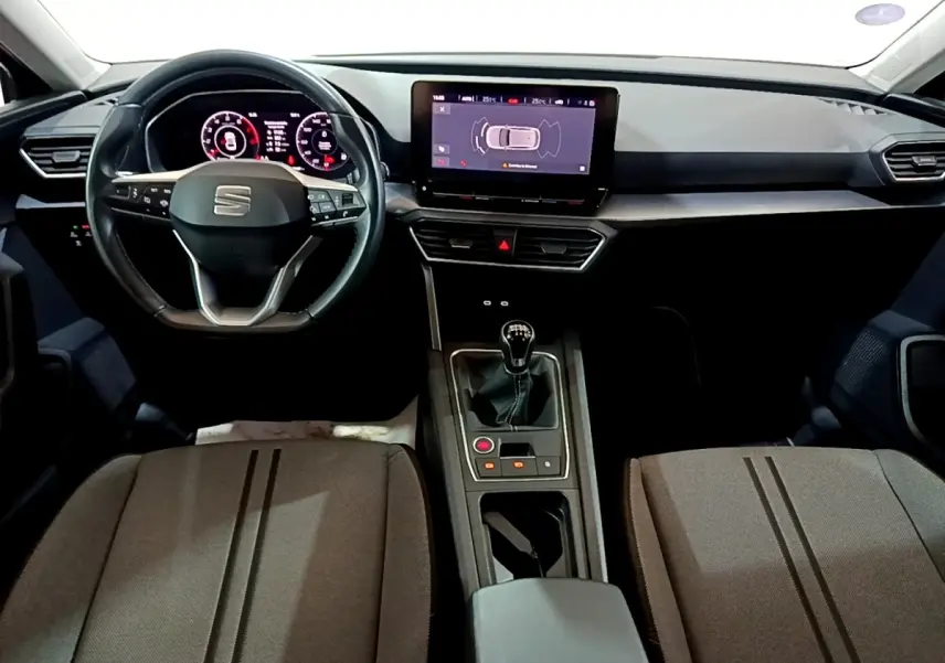 Vue intérieure avant du SEAT Leon 2023 essence gris clair, volant cuir, écran tactile 10 pouces et boîte manuelle.