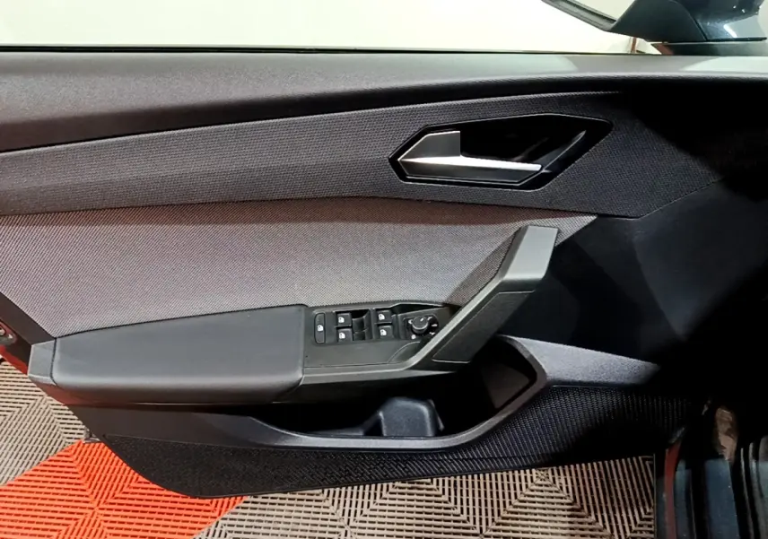 Vue intérieure du panneau de porte avant gauche gris foncé du SEAT Leon 2023 avec commandes électriques des vitres et rétroviseurs.
