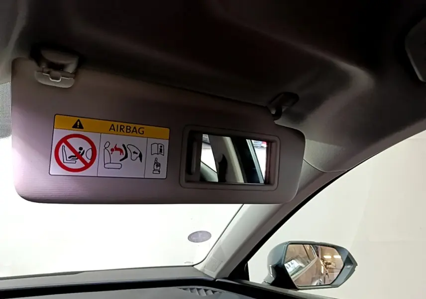 Vue intérieure du pare-soleil côté conducteur avec miroir et avertissement airbag, rétroviseur extérieur gris visible.