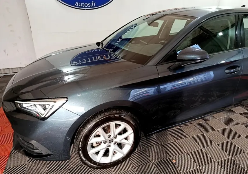 Vue 3/4 avant droit d'une SEAT Leon gris clair 2023 avec phares LED et jantes alliage blanc.