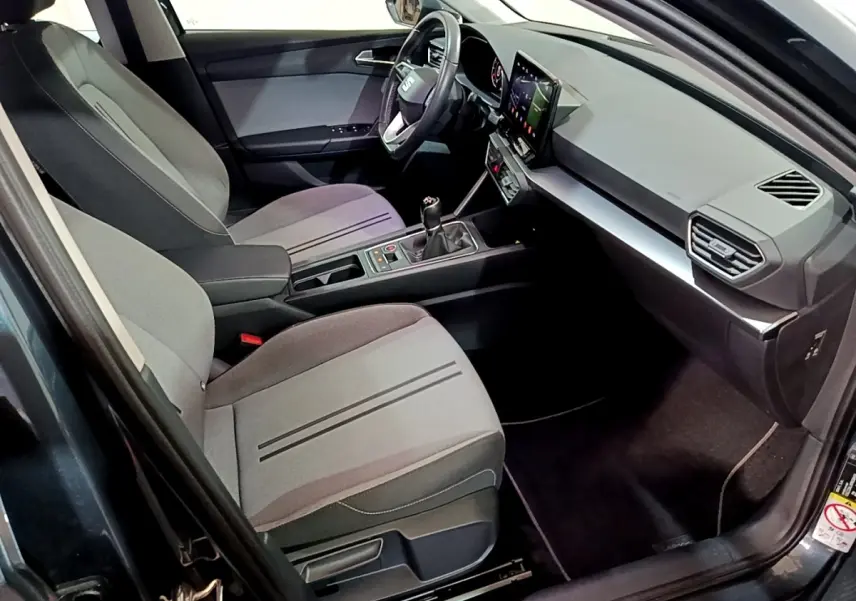 Vue intérieure côté conducteur de la SEAT LEON gris clair 2023 avec tableau de bord moderne et boîte manuelle.