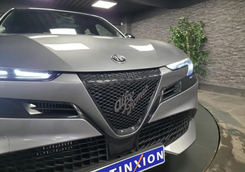 Vue avant rapprochée de l'Alfa Romeo Junior 1.2 hybride gris métallisé avec calandre noire et phares LED allumés.