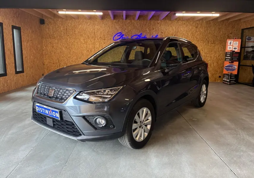 SEAT Arona gris foncé en 3/4 avant droit dans un showroom avec éclairage intérieur et jantes argentées.