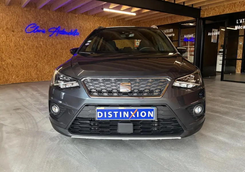 Vue frontale d'un SEAT Arona gris foncé 2021, mettant en valeur sa calandre et ses phares LED dans un showroom.