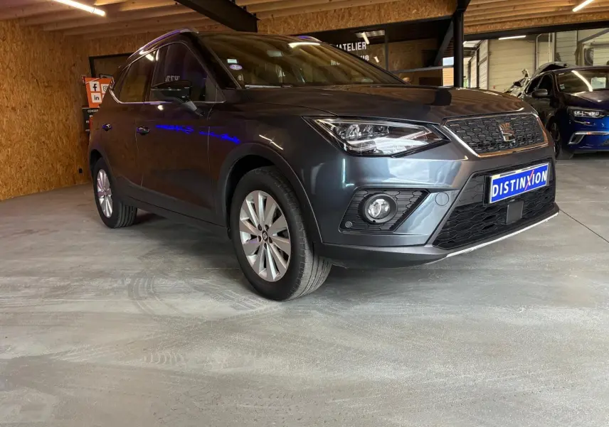 SEAT Arona gris foncé vue 3/4 avant droit dans un garage, avec calandre et phares distinctifs visibles.