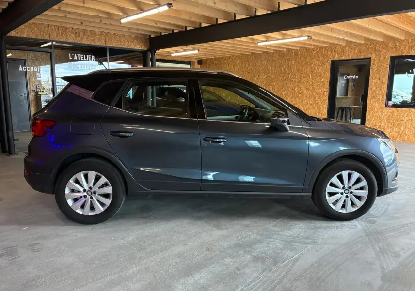 Vue de profil côté gauche d'un SEAT Arona gris foncé 2021 en intérieur, avec jantes argentées et toit noir.