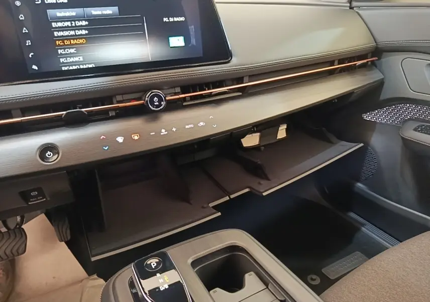 Intérieur du Nissan Ariya 63kWh noir, vue côté passager sur tableau de bord avec boîte à gants ouverte et écran tactile.