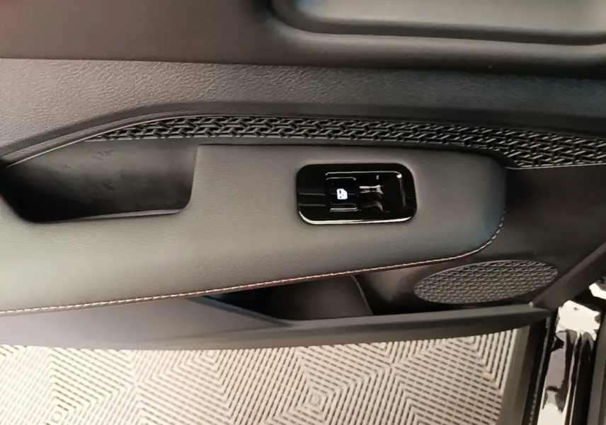 Détail de la porte intérieure côté conducteur du Nissan Ariya noir, montrant la commande de verrouillage et haut-parleur.