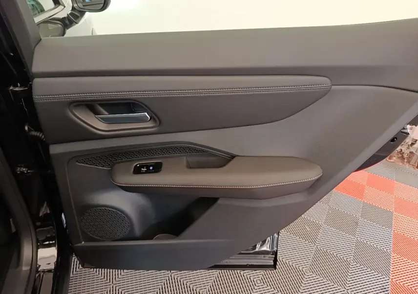 Vue intérieure côté gauche de la porte arrière noire du Nissan Ariya 63kWh avec accoudoir et commandes électriques.