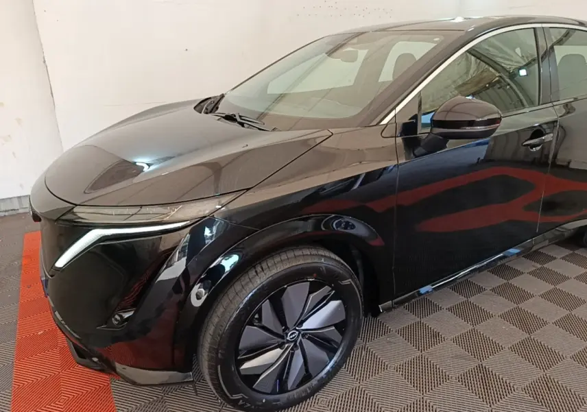 Vue 3/4 avant droit du Nissan Ariya noir 63kWh avec phares LED et jantes design en intérieur fermé.