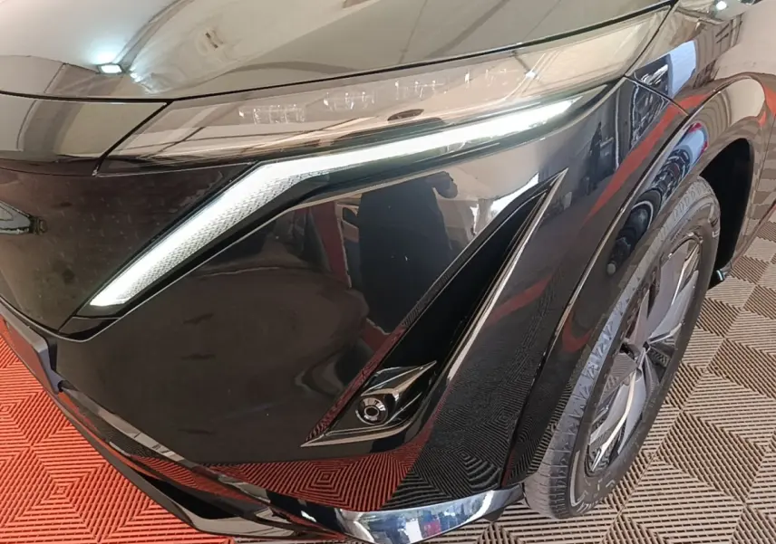 Gros plan sur l'avant droit noir du Nissan Ariya 63kWh 218ch Engage, mettant en valeur le phare LED et la roue.
